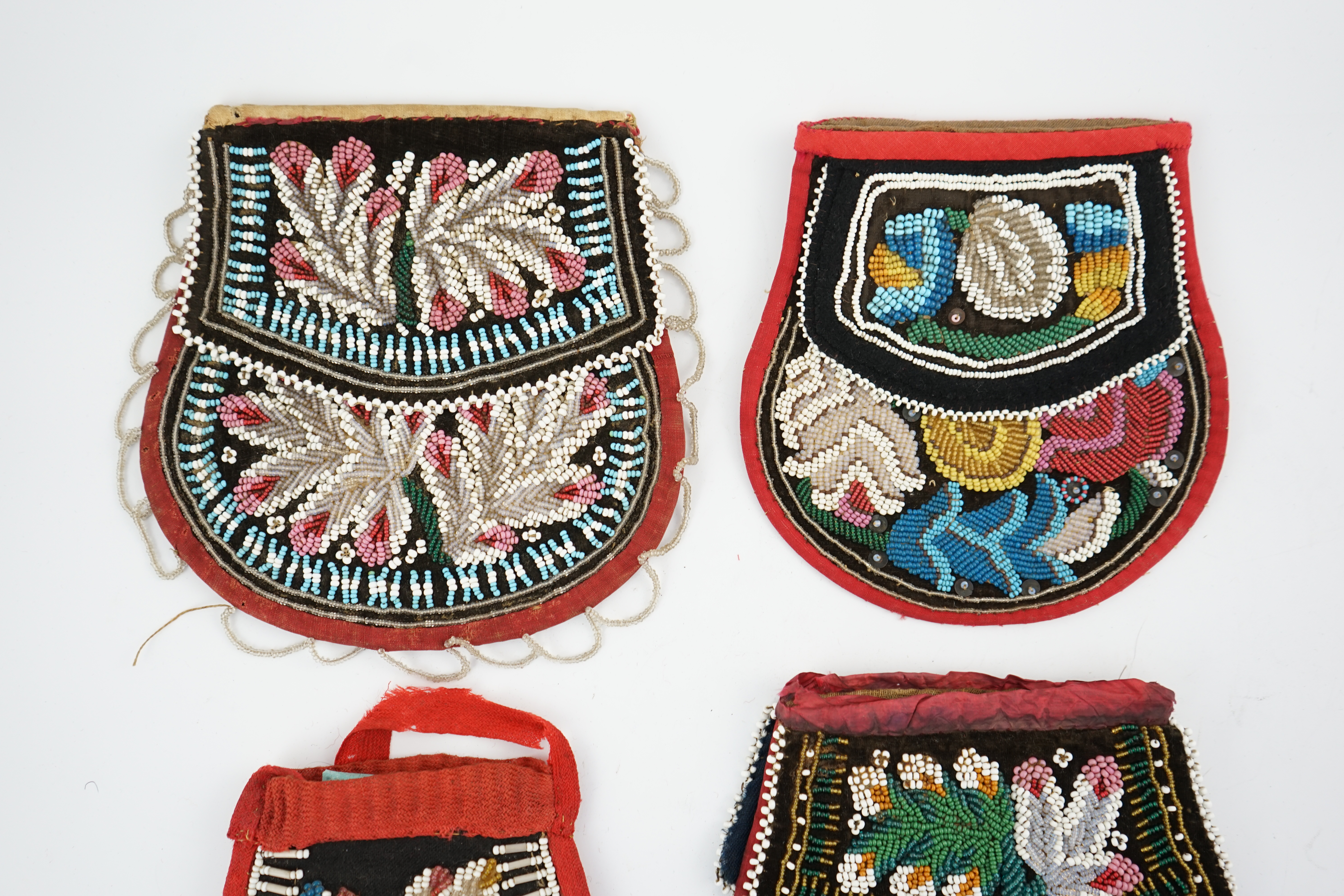 Three 19th century Iroquois Native American beaded bags and a smaller pouch, the bags have beaded flaps, the pouch is shaped with mostly white and turquoise beading having a red fabric edging, all four have very differen